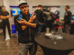 Respawnin teknologiakatsaus – mitä himoita seuraavaksi? Jusku pelleilee kahden juomalasin kanssa messuosastolla.