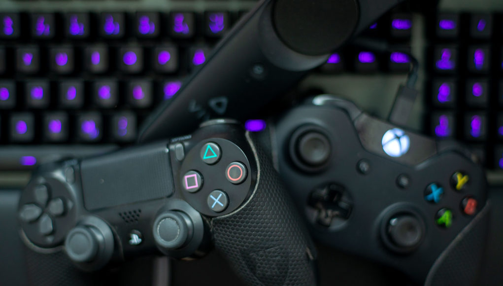 DualShock 4, Xbox One -ohjain, HTC Viven ohjain ja tietokoneen näppäimistö läjässä.