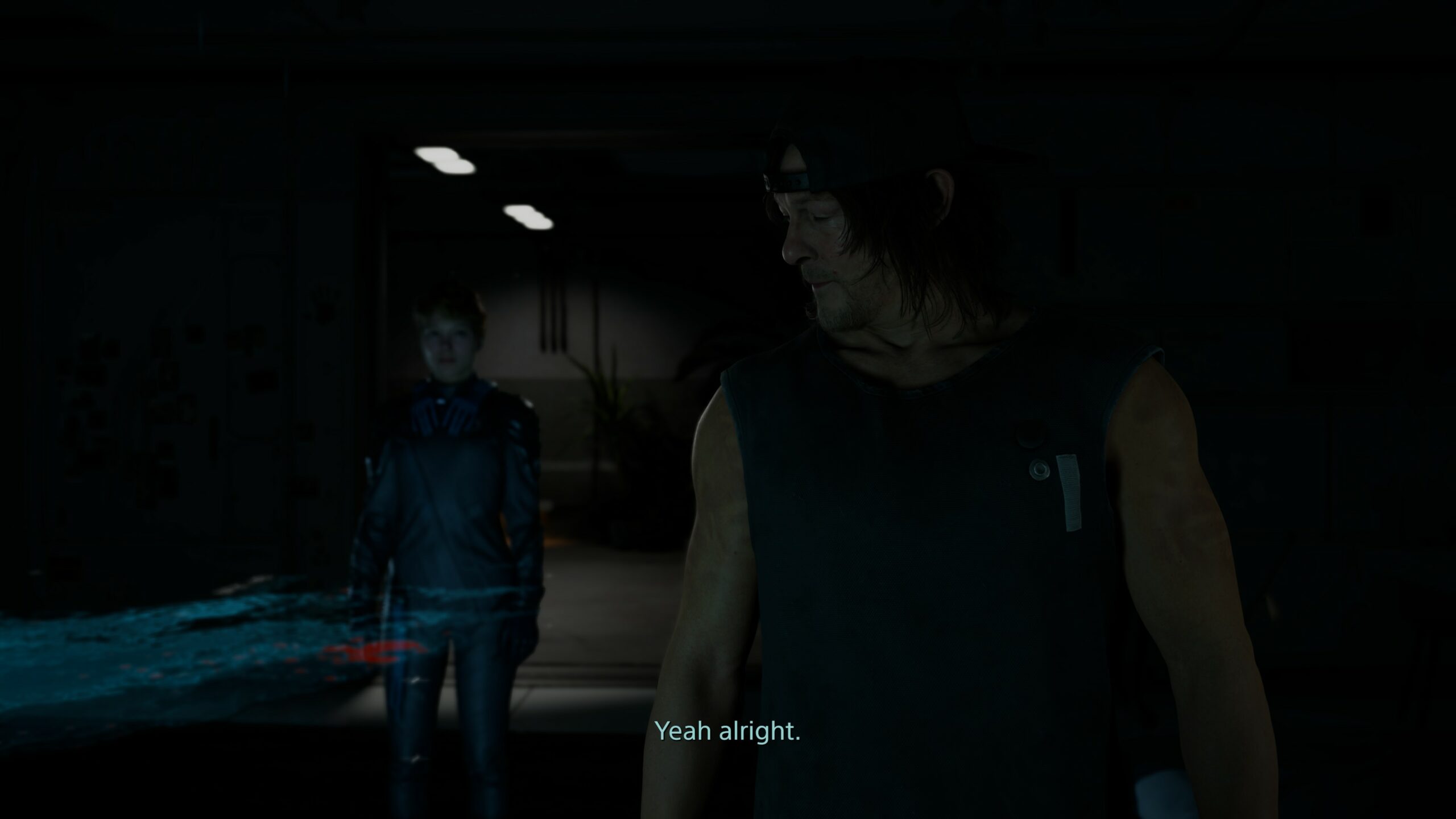 Norman Reedusin esittämä hahmo hämärässä huoneessa, taustalla seisoo toinen henkilö. Alareunassa on tekstitys "Yeah alright."