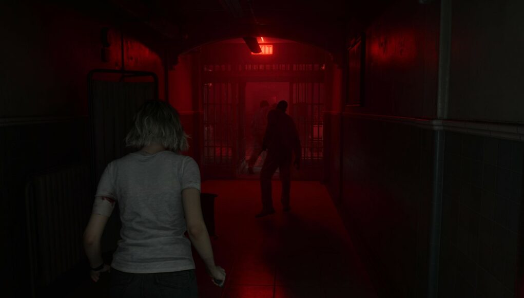 Pelinäkymä hämärästä ja pelottavasta sairaalan tai vankilan käytävästä, jota valaisee vain punainen hätävalo ja EXIT-kyltti. Etualalla on vaaleatukkainen nainen selin, ja käytävän päässä häämöttää kaksi tummaa, uhkaavaa hahmoa kaltereiden takana.