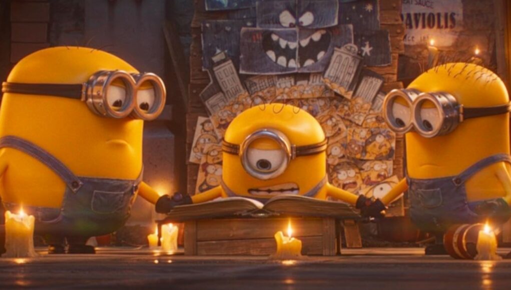 Kolme Kätyrit-hahmoa (Minions) seisoo hämärässä huoneessa pöydän äärellä, jolla on avoin kirja. Keskimmäinen, yksisilmäinen Kätyri lukee kirjaa keskittyneenä, kun taas kaksi muuta pitelevät toisiaan käsistä hänen sivuillaan. Pöydällä ja lattialla palaa useita kynttilöitä, jotka luovat lämmintä valoa. Taustalla näkyy seinä, joka on täynnä piirustuksia ja luonnoiteltuja hahmoja.