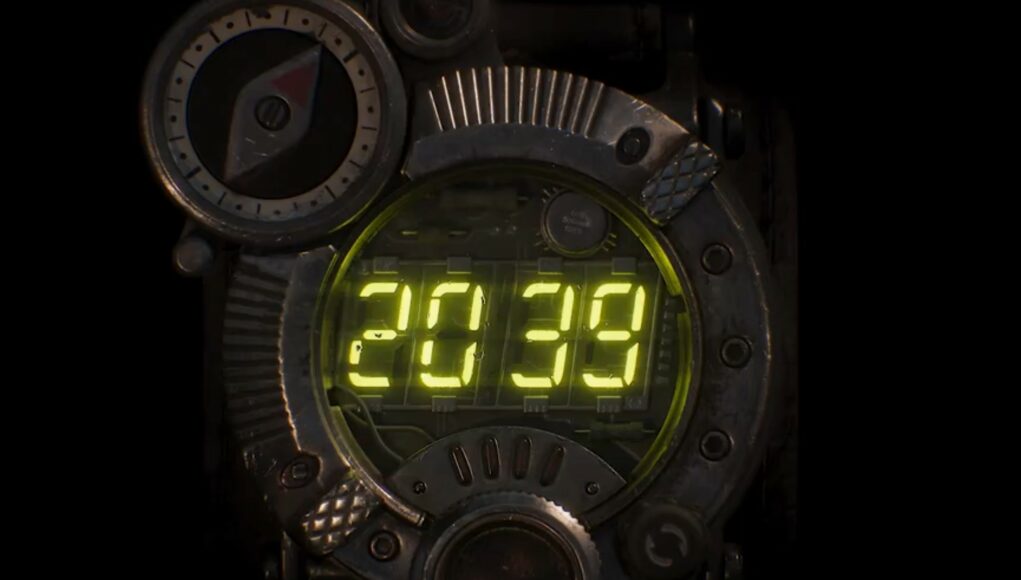 metro-2039-teaserlogo Lähikuva taktisesta rannelaitteesta, jossa on suuri digitaalinen näyttö. Näytöllä loistavat kirkkaankeltaiset numerot ”2039”. Laitteessa on vankka, metallinen runko ja vasemmassa yläkulmassa on pyöreä kompassi, jonka neula osoittaa koilliseen. Tausta on täysin musta, mikä korostaa laitteen valoa ja yksityiskohtia.