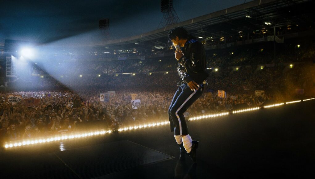 Laaja kuva Michael Jacksonista esiintymässä suurella stadionilla kymmenien tuhansien fanien edessä. Jackson on kuvattu sivuprofiilista lavan reunalla, ja hänellä on yllään tunnusomaiset mustat housut valkoisilla raidoilla, musta takki, valkoiset sukat ja mustat kengät. Hän pitelee mikrofonia ja on dynaamisessa asennossa. Lavan reunalla on kirkas valonauha, ja taustalla näkyy valtava yleisömeri, jota valaisevat stadionin valonheittimet pimeässä illassa.