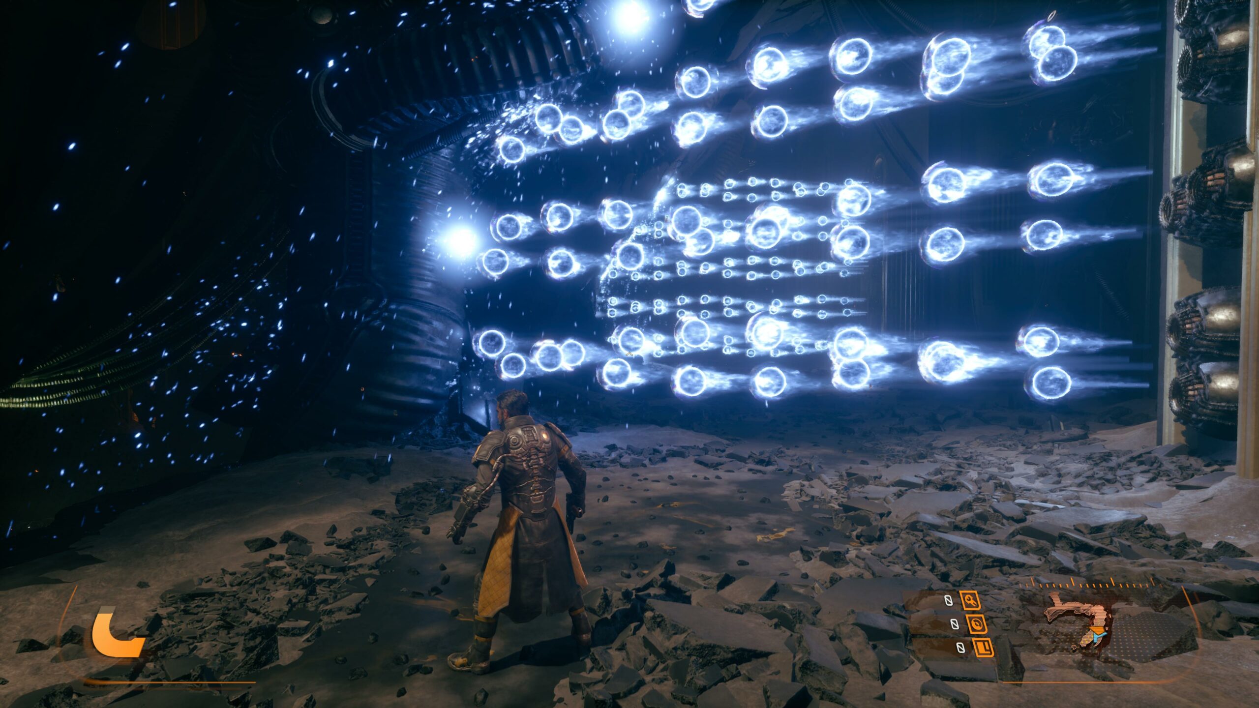 Kolmannen persoonan kuvakaappaus tieteiselokuvamaisesta videopelistä. Pelaajahahmo, jolla on yllään raskaasti varusteltu haarniska ja pitkä keltainen takki, seisoo selin kameraan kivisellä ja hämärällä alustalla. Hänen edessään ilmassa leijuu suuri määrä kirkkaan sinisiä, hohtavia energiapalloja, jotka muodostavat verkkomaisen kuvion pimeässä tilassa. Ruudun alalaidassa näkyy oranssi pelin käyttöliittymä.