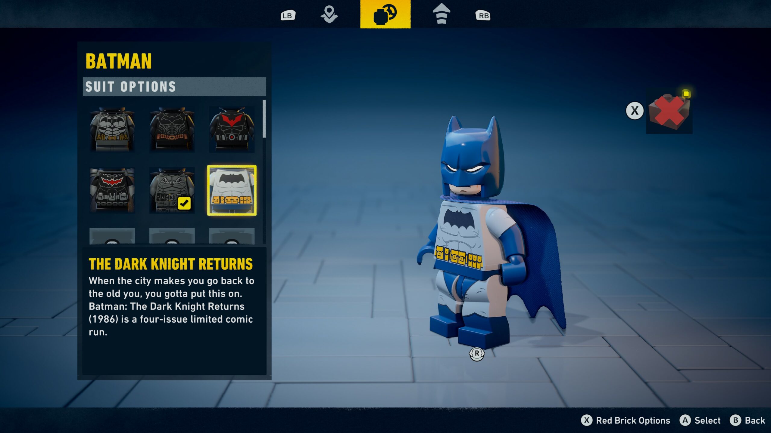 Kuvakaappaus videopelin asuvalintavalikosta (Suit Options). Oikealla puolella on Lego Batman -hahmo pukeutuneena harmaaseen pukuun, jossa on sininen viitta ja naamio sekä keltainen varustevyö. Vasemmalla puolella on valikko, jossa näkyy eri asuvaihtoehtoja ikoneina. Valittuna on asu otsikolla ”THE DARK KNIGHT RETURNS”, ja sen alla on lyhyt kuvausteksti, jossa viitataan vuoden 1986 sarjakuvaan. Ruudun ylä- ja alalaidassa näkyvät peliohjaimen painikesymbolit.