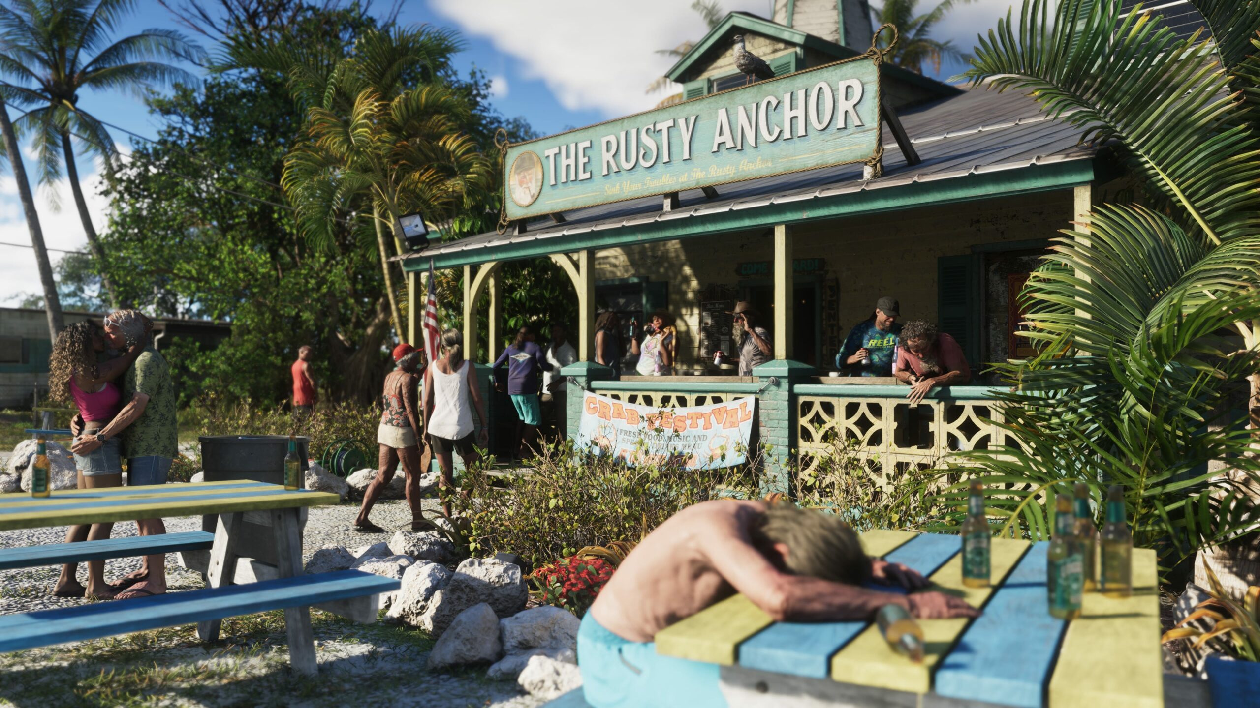 Yksityiskohtainen ruutukaappaus videopelistä, jossa näkyy rannalla sijaitseva baari nimeltä "The Rusty Anchor". Rakennus on puuta, ja sen katolla on suuri kyltti sekä sääasemaa muistuttava torni. Baarin edustalla on trooppisia kasveja, kuten palmuja, ja aurinkoinen sää. Etualalla oikealla mies makaa sammuneena värikkään piknik-pöydän ääressä, jolla on useita olutpulloja. Vasemmalla pariskunta suutelee toisen pöydän luona. Taustalla näkyy muita ihmisiä oleskelemassa baarin terassilla, ja rakennuksen seinässä on mainos "Crab Festival" -tapahtumasta.
