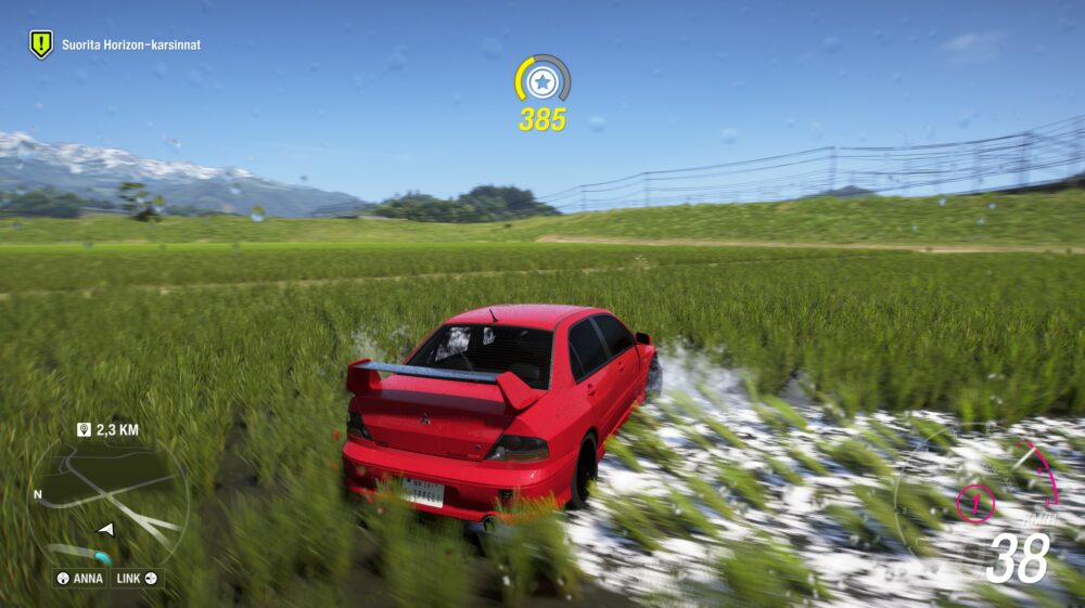 Ruutukaappaus Forza Horizon -ajopelistä, jossa punainen Mitsubishi Lancer Evolution IX driftaa vauhdikkaasti märällä nurmikentällä tai riisipellolla. Renkaista roiskuu valkoista vettä ja mutaa. Taustalla näkyy vihreitä kukkuloita ja lumihuippuisia vuoria kirkkaan sinisen taivaan alla. Pelin käyttöliittymä näyttää 38 km/h nopeuden, minikartan ja pisteitä kertyvän "385" -mittarin. Kameran linssissä näkyy vesipisaroita, jotka simuloivat vesisadetta.