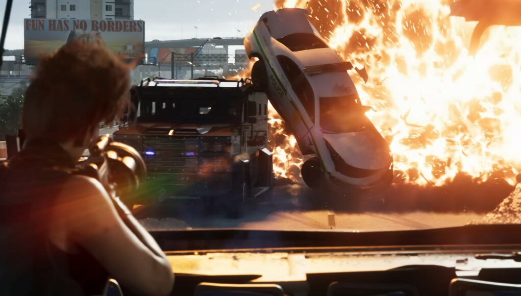 gta6-rajahdys Toiminnallinen ruutukaappaus videopelistä, jossa nähdään suuri räjähdys tiellä. Etualalla on hahmo selin kameraan päin, ja hän pitelee asetta tähdäten kohti tapahtumia. Keskellä kuvaa poliisiauto on lennähtänyt ilmaan valtavan tulipallon voimasta, ja sen vieressä on panssaroitu ajoneuvo. Taustalla näkyy kaupunkimaisemaa ja mainostaulu, jossa lukee "FUN HAS NO BORDERS". Valo on kirkas ja räjähdyksen oranssit sävyt hallitsevat kuvaa luoden dynaamisen tunnelman.