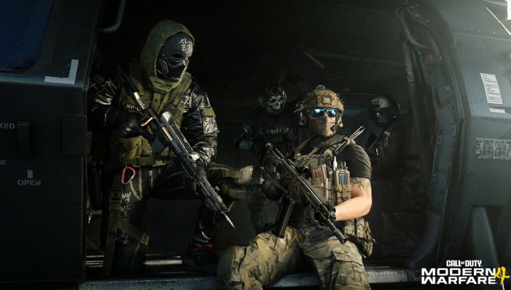 mw4-sotilaat-kopterissa Toiminnallinen julkaisukuva Call of Duty: Modern Warfare III -videopelistä, jossa neljä raskaasti varustautunutta sotilashahmoa istuu ja seisoo sotilashelikopterin avoimella ovella valmiina laskeutumaan. Etualalla oikealla istuu maastokuvioisiin housuihin ja taktiseen liiviin pukeutunut sotilas, jolla on kypärä, aurinkolasit ja rynnäkkökivääri sylissään. Vasemmalla seisoo hahmo, jolla on kasvoillaan musta maski valkoisilla kirjoituksilla, vihreä huppu ja musta kiiltävä takki, ja hän pitelee tarkkuuskivääriä. Helikopterin hämärässä sisätilassa taustalla näkyy kaksi muuta sotilasta, joista toisella on pääkallomaski.