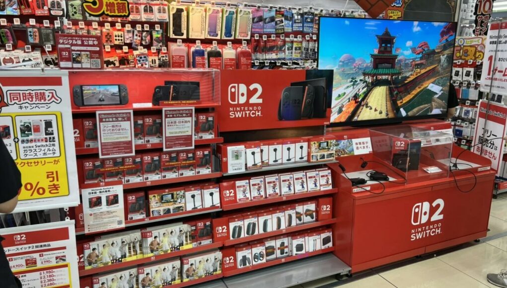 Myymälähylly, jossa on esillä Nintendo Switch 2 -pelikonsoleita, tarvikkeita ja demopiste, jossa pyörii pelikuvaa näytöllä.