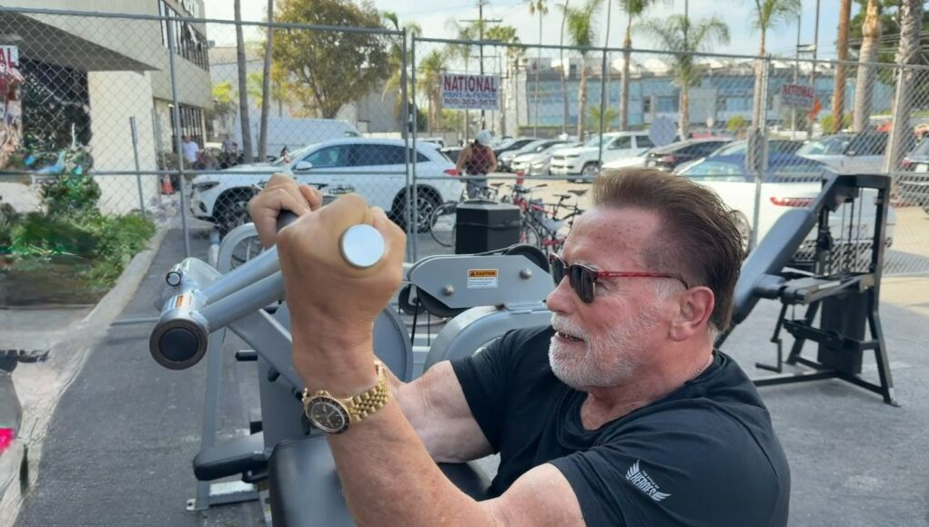 schwarzenegger-79-vuotta Arnold Schwarzenegger treenaamassa ulkokuntosalilla mustassa t-paidassa, aurinkolaseissa ja kultaisessa rannekellossa.