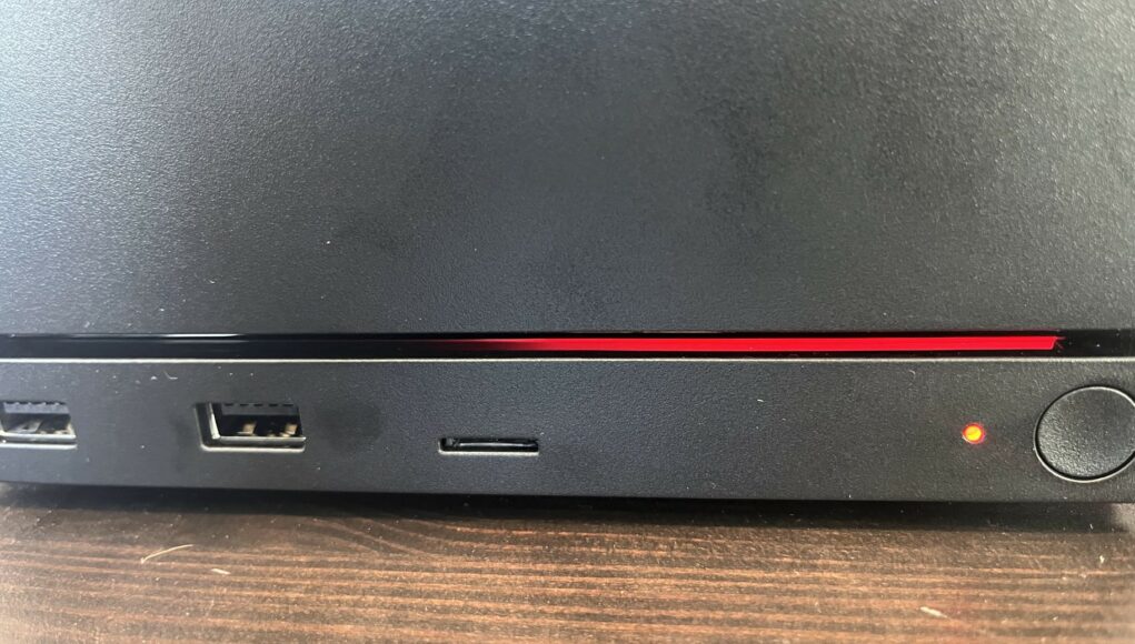 Mustan elektronisen laitteen etupaneeli, jossa näkyy punainen merkkivalo, USB-portteja ja kapea vaakasuora punainen valojuova.