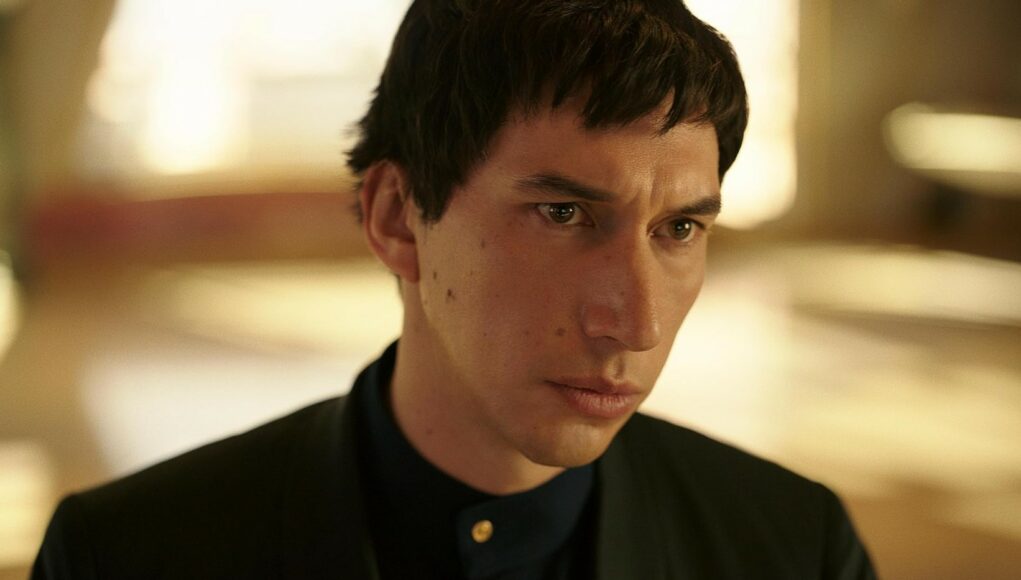 Näyttelijä Adam Driver vakavana ja mietteliäänä tummassa, korkeakauluksessa asussa.