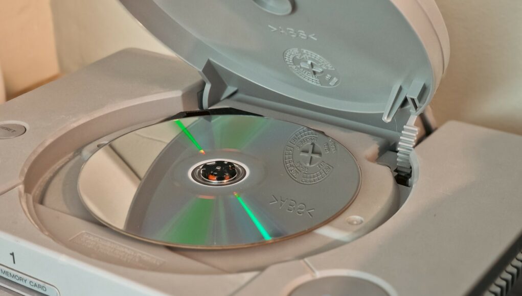 ps1-fyysinen-pelilevy Harmaan PlayStation 1 -konsolin avoin levykelkka, jonka sisällä on pelilevy.