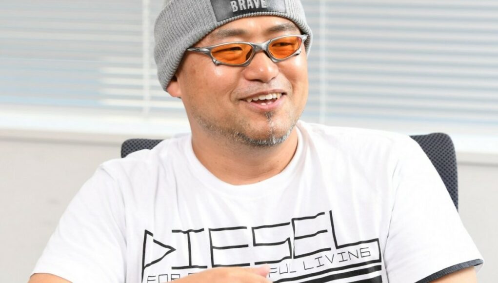 Hideki Kamiya istuu ja nauraa tuolla.