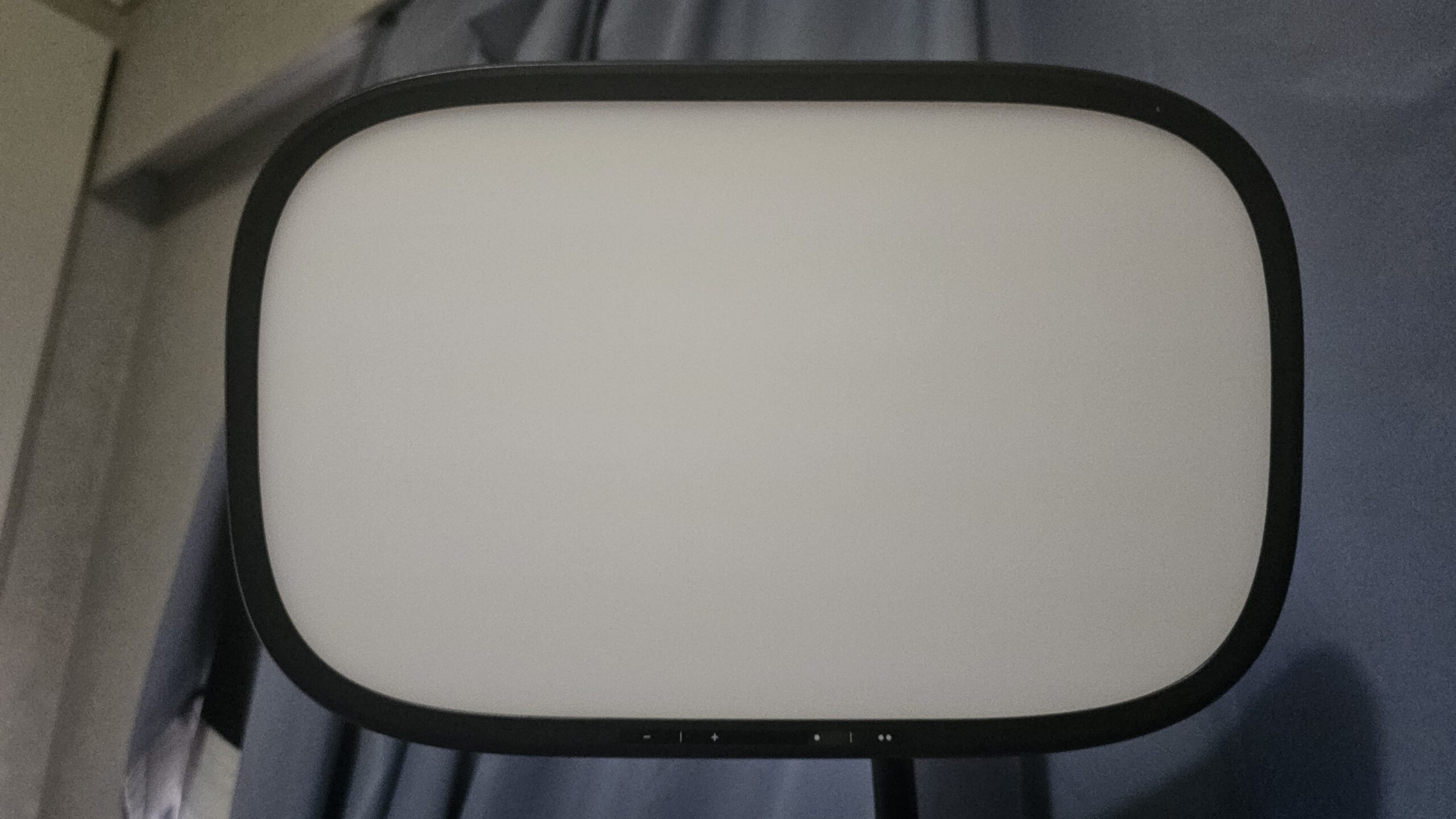 Elgato Key Light Air MK.2 -valopaneeli suoraan edestä kuvattuna valkoista diffuusiopintaa vasten. Pyöristetyn suorakulmion muotoista valoa kehystää ohut musta reunus, jonka alalaidassa näkyvät pienet säätösymbolit.
