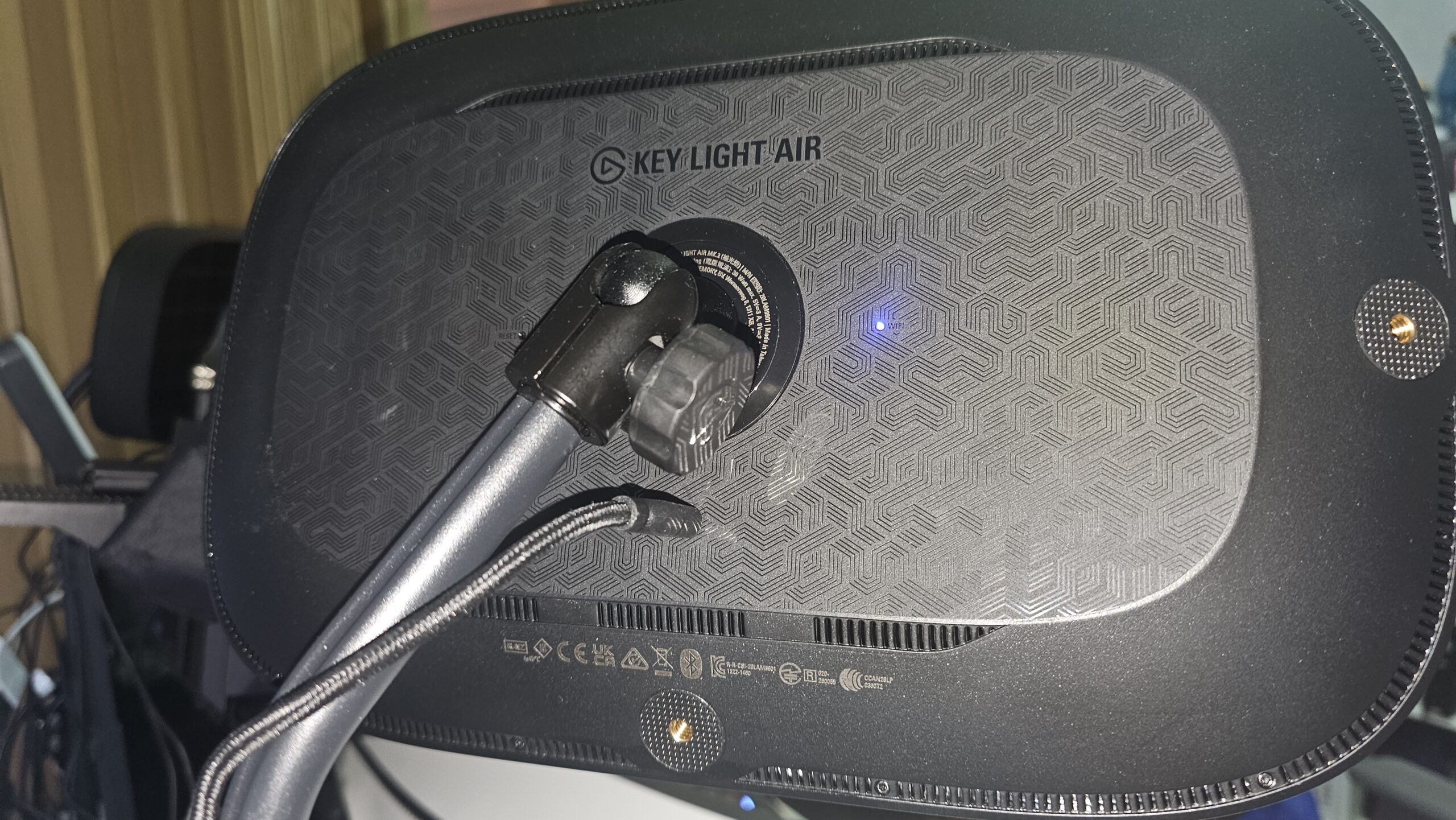 Elgato Key Light Air MK.2 -valopaneelin takapuoli. Mustassa taustassa on tyylitelty geometrinen viivakuviointi, "KEY LIGHT AIR" -teksti, pieni sininen merkkivalo, ruuvikiinnitteinen pallonivel jalustakiinnitystä varten sekä alareunan ilmanvaihtosäleikkö ja liitännät.