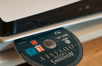 PlayStation saattaa sittenkin pyörtää kiistellyn päätöksensä – tuleeko PS6:een sittenkin levyasema? Lähikuva PlayStation-pelikonsolista, jonka levyasemaan on työnnetty Assassin's Creed Odyssey -pelin blu-ray-levy.
