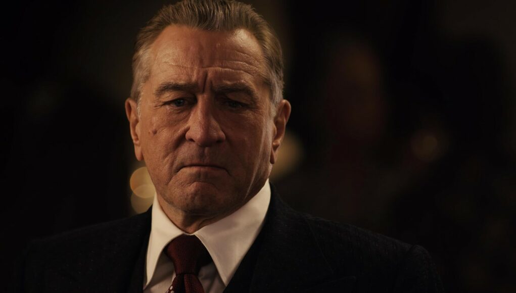 robert-de-niro Lähikuva näyttelijä Robert De Nirosta puvussa, valkoisessa kauluspaidassa ja solmiossa vakavana hämärässä taustassa.