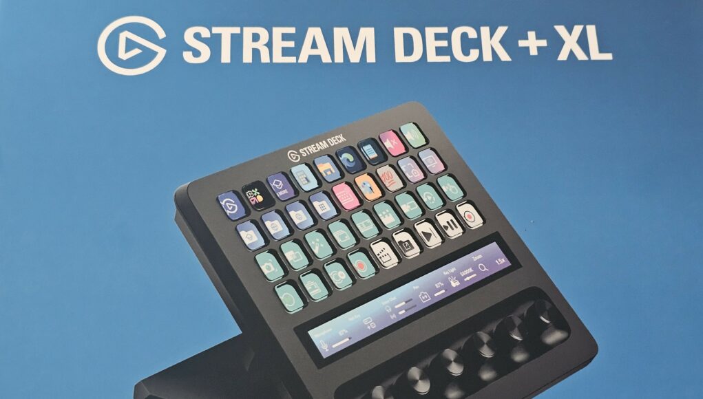 sdpxl_cover Musta Elgato Stream Deck + XL -ohjain sinistä taustaa vasten, yläpuolella valkoinen teksti "STREAM DECK + XL". Laitteen näppäimissä ja kosketusnäytössä on päällä vaaleansävyiset pikakuvakkeet ja liukusäätimet valaistuksen ja mikrofonin hallintaan.