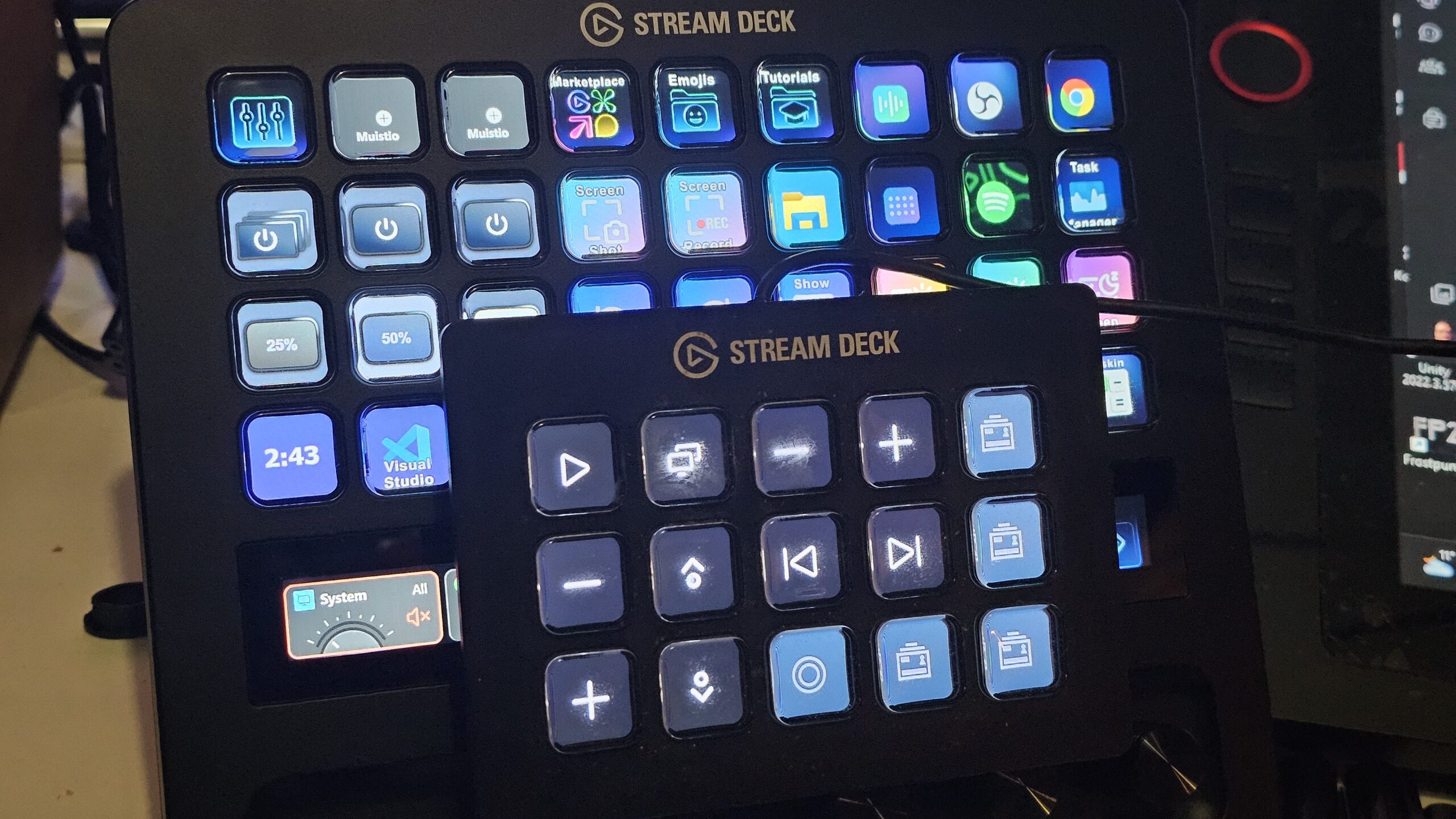 Pienempi, 15-painikkeinen perinteinen Stream Deck -ohjain sinisillä mediapainikkeilla asetettuna suuren ja monipuolisemman Elgato Stream Deck + XL -ohjaimen päälle havainnollistamaan laitteiden kokoeroa ja näppäinasettelua.