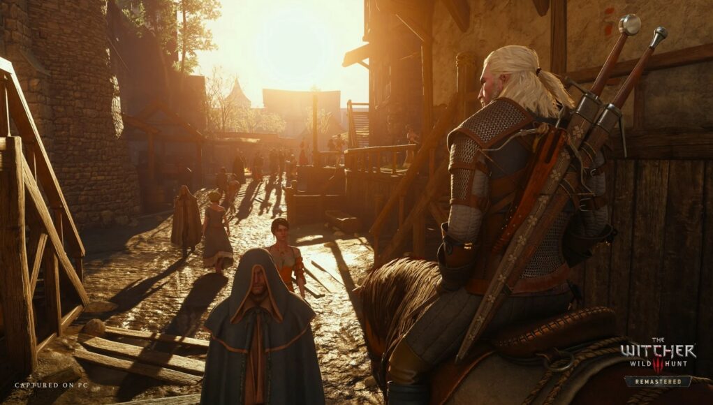 witcher-3-remastered The Witcher 3: Wild Hunt Remastered -pelin kuvakaappaus, jossa valkohiuksinen noituri Geralt ratsastaa hevosella halki keskiaikaisen kylän katuosuuden ilta-auringon lämpimässä valossa, selässään kaksi miekkaa ja taustalla näkyy muita kyläläisiä.