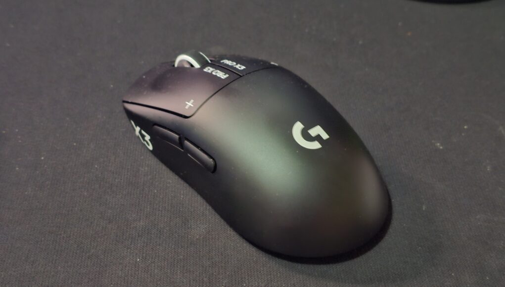1 Musta Logitech G Pro X3 Prostrike -pelihiiri kuvattuna viistosti edestä tummalla hiirimatolla. Päänäppäimissä näkyvät valkoiset PRO X3- ja plus-merkinnät sekä kuvioitu rullapyörä, kyljessä kaksi peukalopainiketta ja kämmenosassa valkoinen Logitech G -logo.