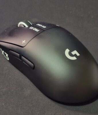 Logitech Pro X3 Superstrike -pelihiiren arvostelu – hiotumpi Superstrike 1.5 Musta Logitech G Pro X3 Prostrike -pelihiiri kuvattuna viistosti edestä tummalla hiirimatolla. Päänäppäimissä näkyvät valkoiset PRO X3- ja plus-merkinnät sekä kuvioitu rullapyörä, kyljessä kaksi peukalopainiketta ja kämmenosassa valkoinen Logitech G -logo.