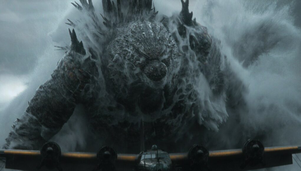 godzilla-minus-zero-lentokone Elokuvakohtaus, jossa massiivinen Godzilla nousee vedestä ja vaahtoavien aaltojen keskeltä nelimoottorisen lentokoneen takana.