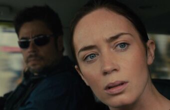 Pitkään odotettu jatko-osa ottaa askeleen eteenpäin – Sicario saa jatkoa Elokuvakohtaus autosta, jossa etualalla vakavalta näyttävä näyttelijä Emily Blunt katsoo suoraan eteenpäin ja taustalla aurinkolaseihin pukeutunut Benicio del Toro istuu tarkkaavaisena auton matkustamossa.