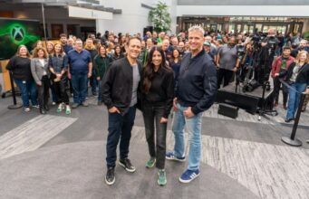 Microsoftilta suora vastaus Xboxia koskeviin huhuihin Ryhmäkuva, jossa Xbox-johtajat Matt Booty, Asha Sharma ja Phil Spencer poseeraavat studiossa tai tapahtumatilassa yleisön edessä.